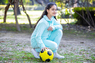 Portrait of young indian girl sitting with soccer or football in the park garden outdoor looking at...
