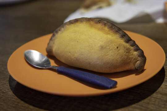 Traditional savory pastry of Cochabamba called saltena on an orange plate with a spoon