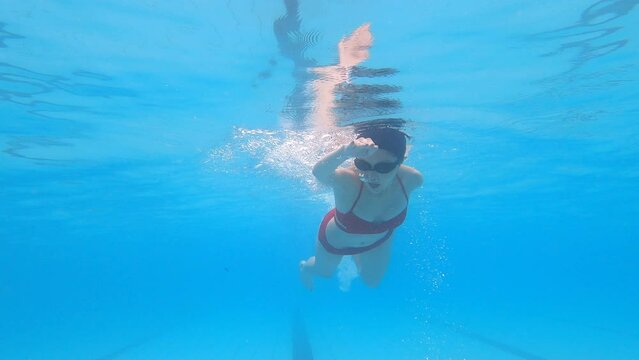 Young woman swimming in free style pose in the pool underwater