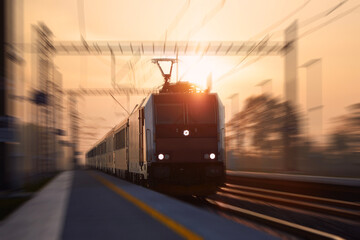 Passenger train fast passing through railroad station. Railway at sunrise with blur effect.. - obrazy, fototapety, plakaty