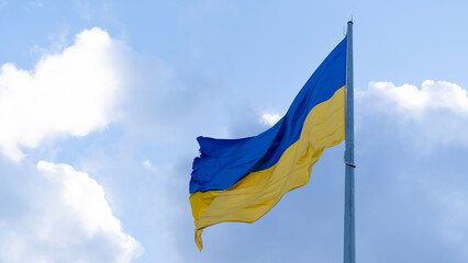 The Ukrainian flag on the flagpole flutters against the background of a blue sky with clouds. Concept: Ukrainians' struggle for independence, the war between Ukraine and Russia.