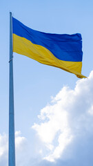 The Ukrainian flag on the flagpole flutters against the background of a blue sky with clouds. Concept: Ukrainians' struggle for independence, the war between Ukraine and Russia.