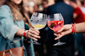 Two women holding a gin and tonic and toasting during a music festival - obrazy, fototapety, plakaty