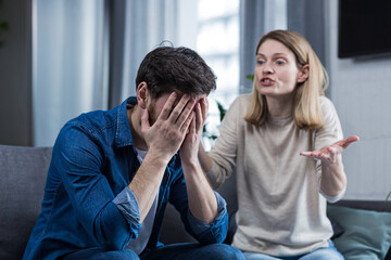 Family conflict, quarrel, misunderstanding. The woman shouts at her husband, in despair, crying. requires explanation. The man listens, covering his face with his hands. Sitting on the couch at home.