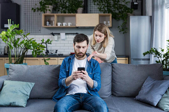 Conflict, young couple, family, man and woman. An angry woman shouts at a man who constantly uses and plays on the phone, does not pay attention - Powered by Adobe