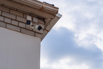 Outdoor surveillance cameras on the old wall under the roof canopy against the blue sky. Outdoor CCTV monitoring, security cameras