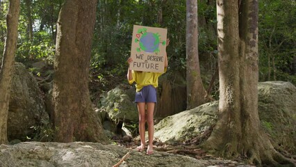 Child girl demonstrates a poster, we deserve a future, in the background of a tropical forest. Poster showing a sign protesting against pollution in the forest. The concept of World Environment Day.
