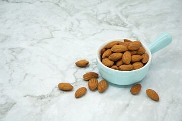 Almonds in bowl on marble background .