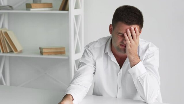 Exhausted work. Suffering man. Headache frustration. Feeling bad sick guy holding head massaging nose bone taking over spectacles sitting desk light room interior.