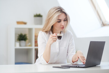 Fototapeta na wymiar Young beautiful caucasian blonde woman working on laptop at home and drinking coffee. Remote work or freelance.