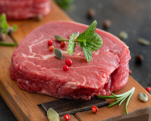 Raw beef fillet steaks with herbs and spices on wooden board on dark background close up