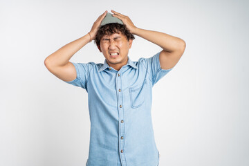Stressed asian young man holding his head over isolated background