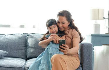 Asian grandmother happy using smartphone taking a selfie photo granddaughter together in the living room.