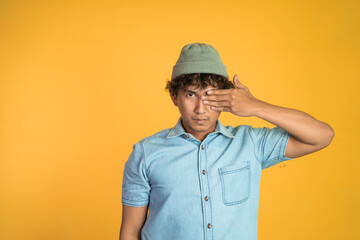 young man with hands covering eyes standing with isolated background. careless and afraid concept