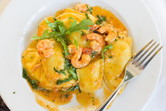 Acciaroli, Italy. Plate of pumpkin stuffed ravioli, with shrimp, in a plate with fork on a restaurant table.