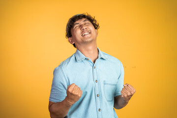 excited asian man with two hands clenched on isolated background. success young man