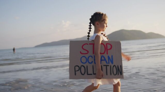 Young girl walking at the seaside with the poster Stop ocean pollution. Environmental Issue, Conservation and Green Politics. Volunteerism, Ecology, Cleaning, Local Clean Up concept.