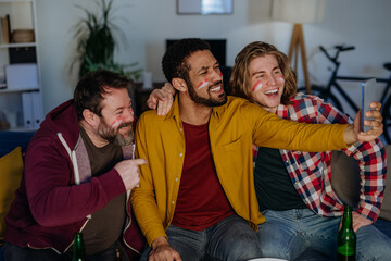 Obraz premium Happy football fans friends watching football at home and taking selfie