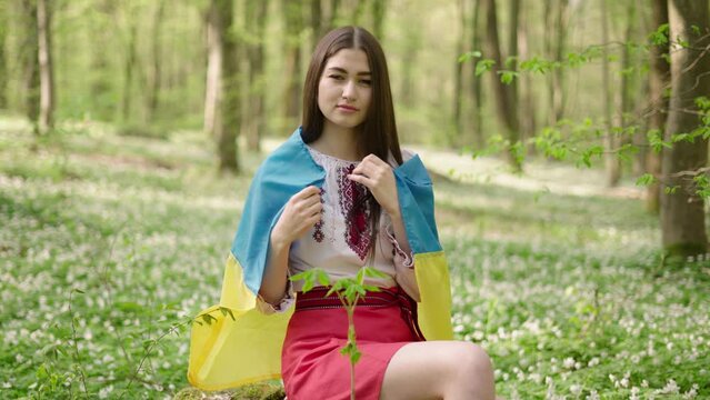 4k shot of young beautiful Ukrainian woman in vyshyvanka  - ukrainian national clothes. She is looking at camera and holding flag - symbol of freedom and independence. Stand with Ukraine  