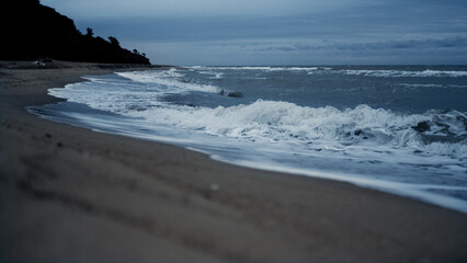 Sea waves splashing sandy beach line in evening ocean view. Dark water concept