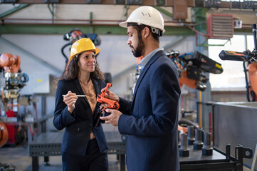 Man engineer holding model of industrial robotic arm and showing to collegue in factory.