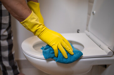 man wearing gloves clean the toilet with a sponge in the bathroom