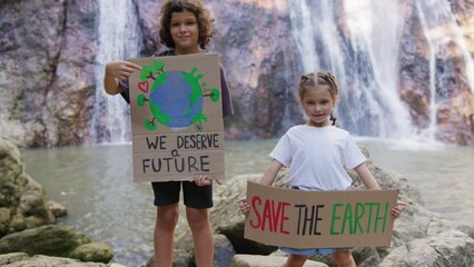 Children at a demonstration in nature with banners in their hands in the background of the waterfall. World environment day concept. Save the planet earth, we deserve a future slogan. - Powered by Adobe