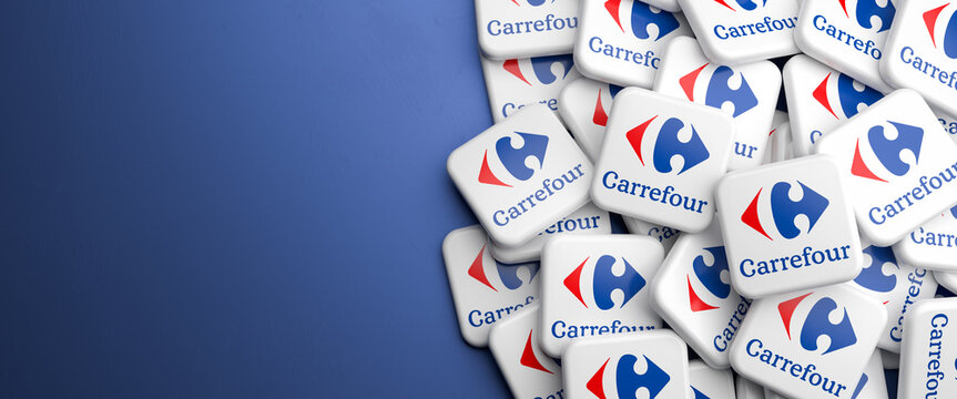 Logos of the French supermarket chain Carrefour on a heap on a table. Copy space. Web banner format.