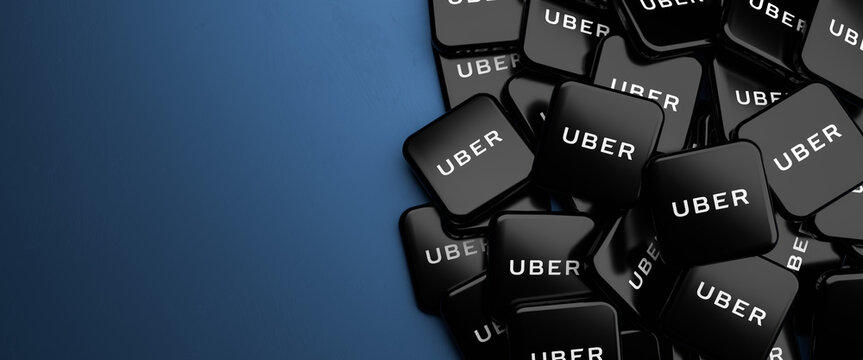 Logos of the mobility service provider, food delivery, scooter rental service Uber on a heap on a table. Copy space. Web banner format.
