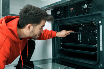 Built-in oven, the young man opens the oven door and prepares for the meal, handsome young man is cooking his own food
