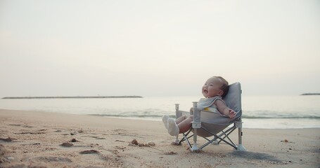 happy cute adorable Asian baby infant sitting relaxing on little chair and smiling with waves on...