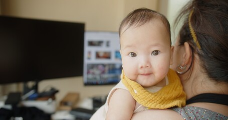 little cute Asian newborn baby infant looking at camera while mother trying working from home,...