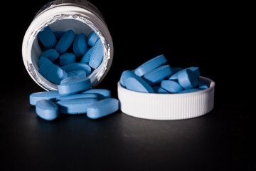 Blue pills in the white plastic container and on the foreground out of focus blue tablets come out and put in the cap