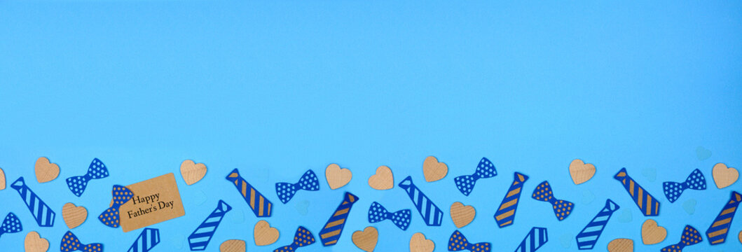 Happy Fathers Day gift tag with bottom border of paper tie decorations and wood hearts on a blue paper banner background. Top down view with copy space.