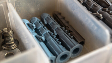 Bolts with disk in plastic box. Metal bolts close up. Long bolts. Long metal bolts. Shining bolts and nuts, blue toned photo. Metal bolts close up. Plastic dowels