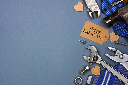 Happy Fathers Day gift tag with side border of ties and tools on a blue grey paper background. Top view with copy space.
