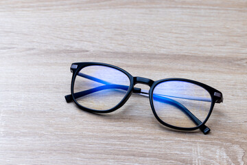 Fototapeta na wymiar Pair of classic black reading glasses on wooden table. Glasses with filter coating blocking screen's blue light to prevent computer vision syndrome (CVS) or digital eye strain.