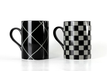 Two black mugs with stripes and checkered pattern isolated on a white background 
