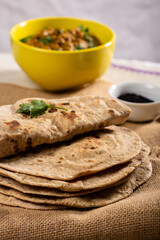 Indian paratha on burlap and yellow bowl with curry in the background