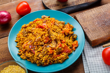 A large dish of bulgur with vegetables and mushrooms in spices on the table.