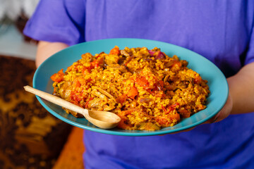 A dish with bulgur and vegetables and a wooden spoon in female hands.