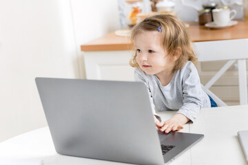 Little beautiful girl study at home while quarantine. Cute child doing homework online sitting in the kitchen . The concept of learning at home for schoolchildren. Distant study concept