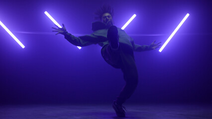 Hiphop performer making tricks on stage. Active man freestyling in ultraviolet.