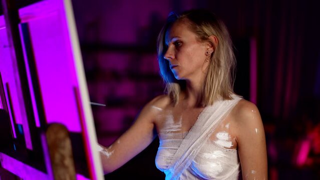 modern european artist woman with tightened breasts by bandages is drawing in dark studio
