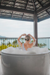 Young woman enjoy bathing in a bathtub with soap bubbles, Luxury jacuzzi suite for relaxation on balcony with landscape of sea view, Samui, Thailand