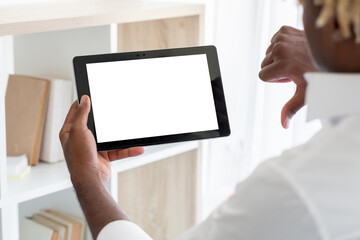 Online meeting. Black man. Digital mockup. Displeased unrecognizable guy holding tablet computer with blank screen showing thumb down light room interior.