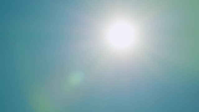 Beautiful sparkle sun moves across clear blue sky. Sun rays light isolated on blue background. Real time.