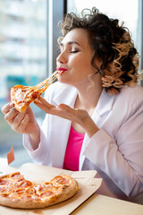 A young woman in a white suit eats delicious pizza