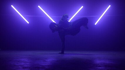 Stylish dancer breakdancing wearing street wear at ultraviolet. Guy moving legs.