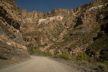 Traveling into the desert. View of the dirt road across the arid environment, rock and sandstone mountains.